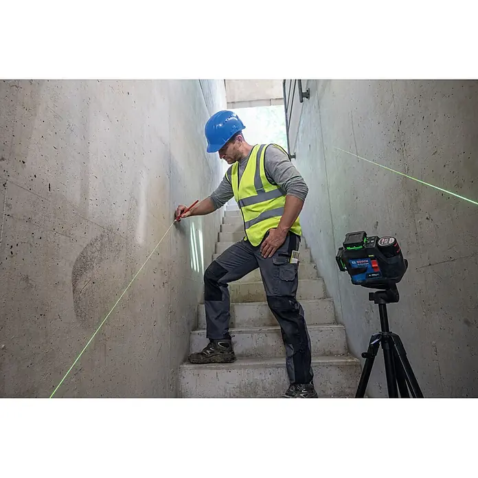 Bosch Professional Linienlaser GLL 12V-100-33 CG PRO - Max. Arbeitsbereich: 30 m - Ein Bauarbeiter verwendet ein Bosch Professional grünes Laser-Nivelliergerät auf einem Stativ, um eine präzise Linie an einer Betonwand zu markieren.