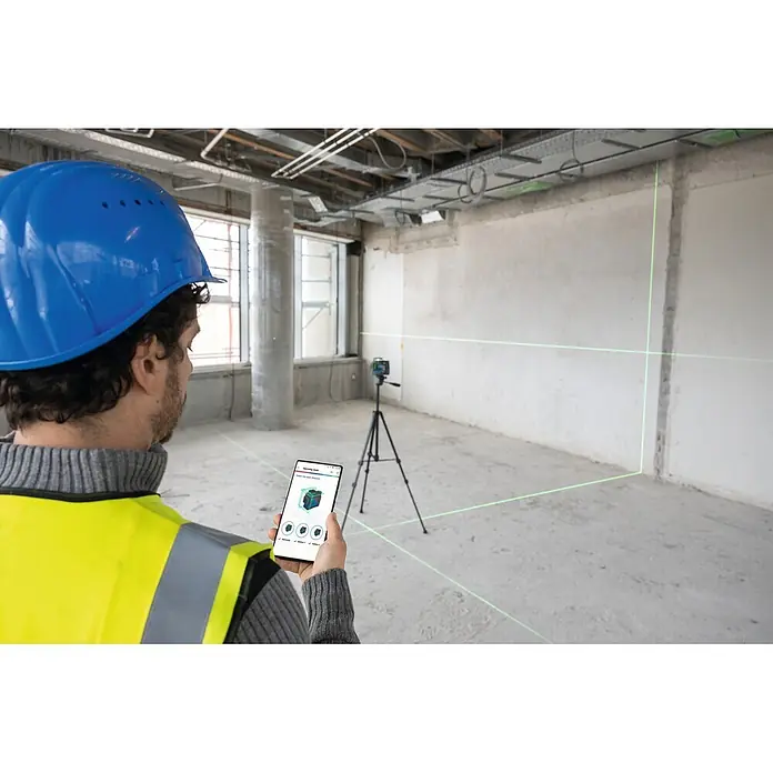 Bosch Professional Linienlaser GLL 12V-100-33 CG PRO - Max. Arbeitsbereich: 30 m - Bauarbeiter steuert grünes Kreuzlinienlaser mit Smartphone in einem Rohbau.