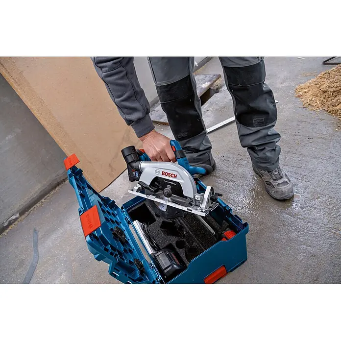 Bosch Professional Akku-Handkreissäge - 18 V, 2 Akkus, Durchmesser Sägeblatt: 165 mm, 5.000 U/min - Person legt eine silberne und blaue Bosch Handkreissäge mit schwarzem Sägeblatt in den passenden blauen Werkzeugkoffer.