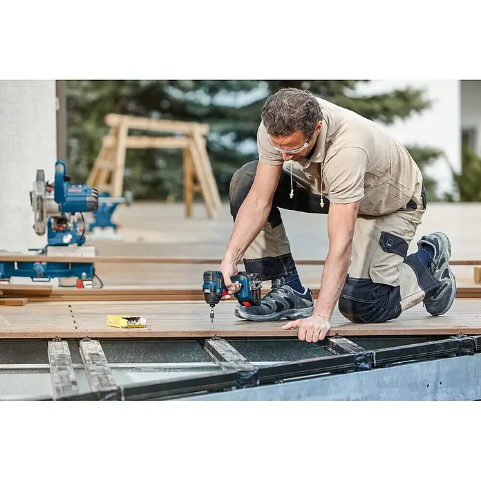 Bosch Professional AMPShare 18V Akku-Drehschlagschrauber GDR 18V-200 - 18 V, Ohne Akku, 200 Nm, Karton - Mann verschraubt braune Terrassendielen mit einem blauen Akku-Schlagschrauber.
