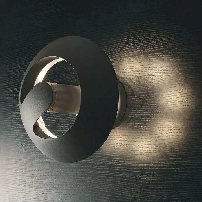 Lutec Aplique exterior LED Spril - 8,4 W, 19,5 x 19,6 x 16,6 cm, Antracita, IP54 - Lámpara de pared LED moderna con diseño circular y luz blanca cálida, ideal para interiores elegantes. La luz destaca la textura de la pared.
