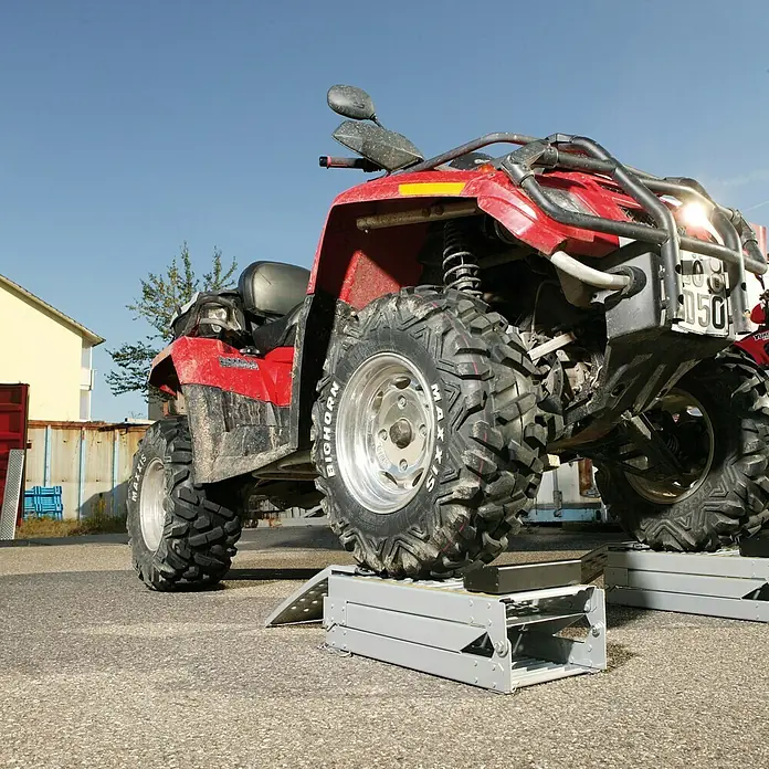 UniTEC Auffahrrampen-Set - Klappbar, 2 Stk., 200 x 23 cm - Das rote Quad steht auf einer grauen Hebebühne, wobei die robusten Reifen und die robuste Bauweise des Fahrzeugs hervorgehoben werden.