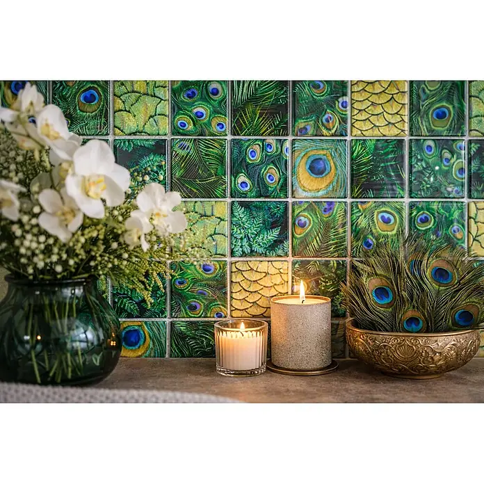 Mosaikfliese Crystal Wildlife XCM WL88 - 29,8 x 29,8 cm, Grün, Glänzend - Eine dekorative Anordnung mit weißen Orchideen, zwei brennenden Kerzen und einer Goldschale mit Pfauenfedern, vor einer grün gemusterten Fliesenwand.