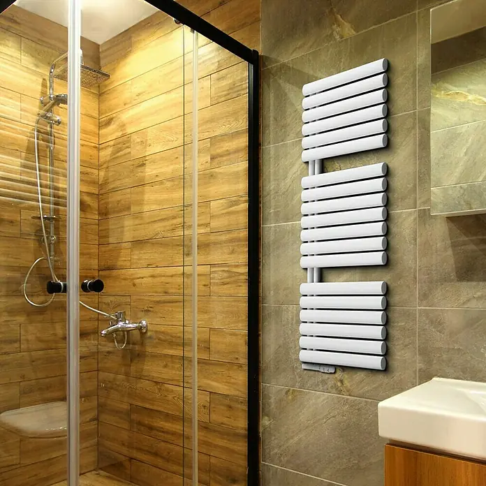 Camargue Designheizkörper Flag Bis - B x H: 600 x 1.216 mm - Das Bild zeigt einen modernen, weißen Handtuchwärmer im Badezimmer, der an einer gefliesten Wand neben einer Dusche und einem Waschbecken montiert ist.