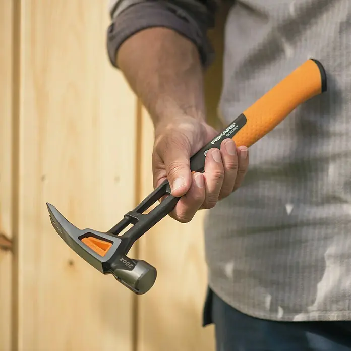 Fiskars Universalhammer XL - Gewicht Kopf: 570 g, Länge: 390 mm - Nahaufnahme eines Mannes, der einen Fiskars IsoCore Hammer mit orangem Griff und schwarzem Kopf hält.