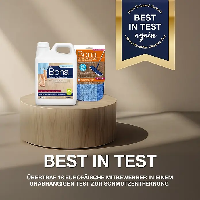 Bona Parkettreiniger - 2,5 l, Nachfüllkanister - Bona 2,5L Holzreinigerflasche und verpacktes blaues Mikrofaser-Reinigungspad auf einem Holzständer, mit „Best in Test“-Auszeichnung.