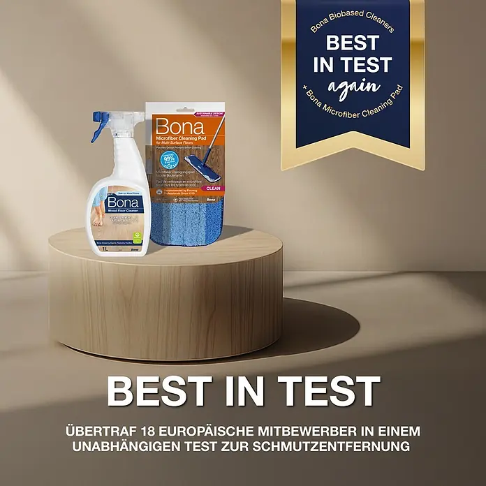 Bona Parkettreiniger - 1 l, Flasche mit Sprühpistole - Weiße Bona Holzbodenreiniger Sprühflasche und blaues Bona Mikrofaser-Pad auf Holzpodest. Mit 'BEST IN TEST' Banner.