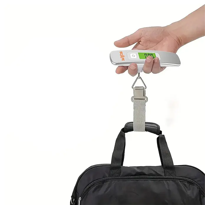 Scape Báscula digital de cocina - Capacidad de carga hasta 50 kg - Mano sosteniendo una báscula digital plateada para equipaje pesando una bolsa de viaje negra.