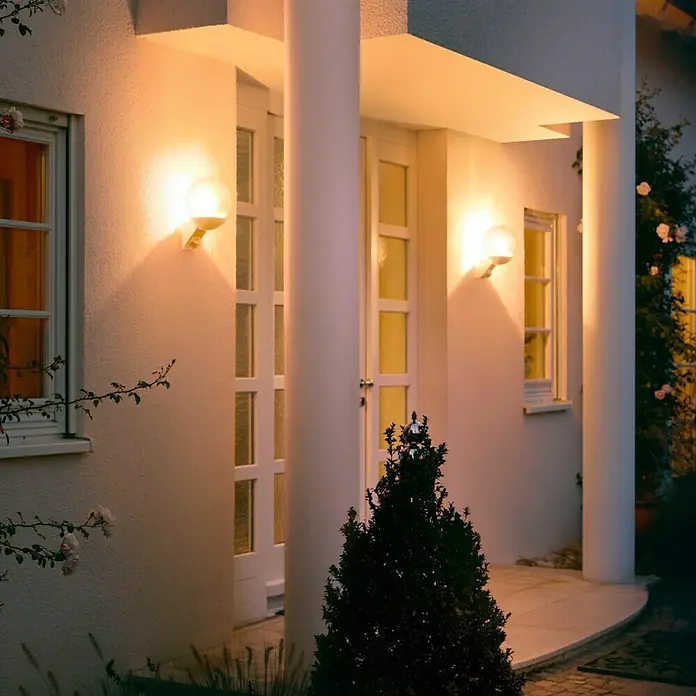 Steinel Sensor-Außenleuchte L 585 S weiß - 60 W, 22,8 x 21,5 x 30,7 cm, Weiß, IP44 - Außenansicht eines Hauses mit runden Wandleuchten, die ein warmes Licht ausstrahlen und die Fassade beleuchten.
