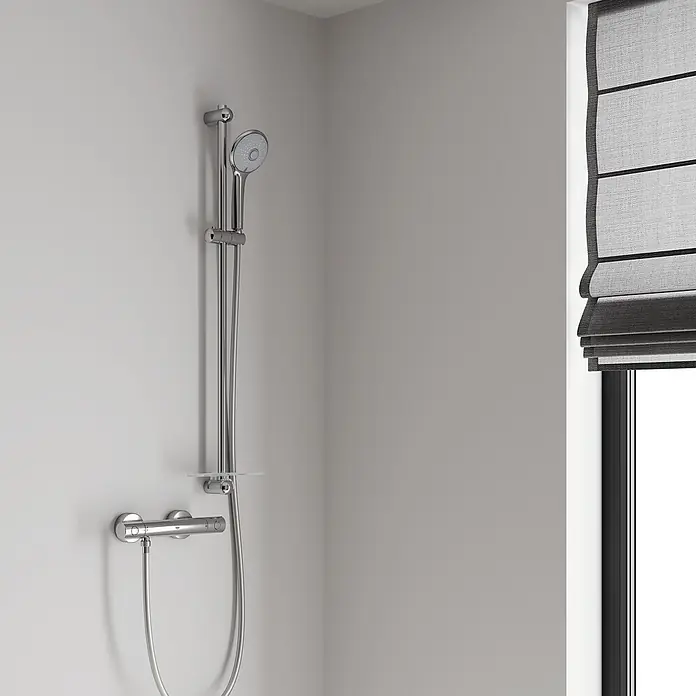 Grohe Euphoria 110 Conjunto de ducha - Distancia entre orificios: 77 cm - 92 cm, Tipos de chorro: Chorro de lluvia, chorro de masaje, SmartRain, Cromo - Sistema de ducha cromado con ducha de mano, barra ajustable y mezclador termostático, instalado junto a una ventana.