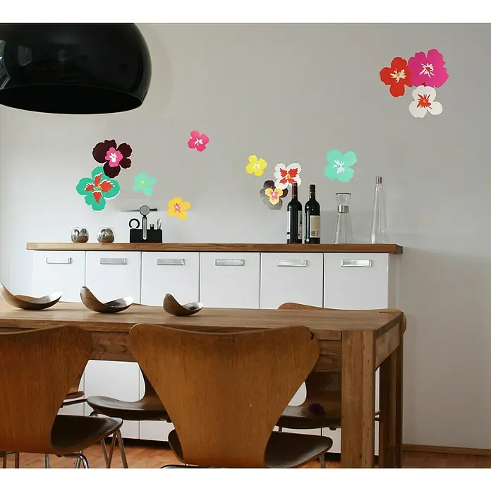 Vinilo de pared Ibiza - 24 x 68 cm, Multicolor, Plástico - Una mesa de comedor con sillas de madera frente a un aparador con calcomanías de flores coloridas en la pared, iluminada por una lámpara negra.