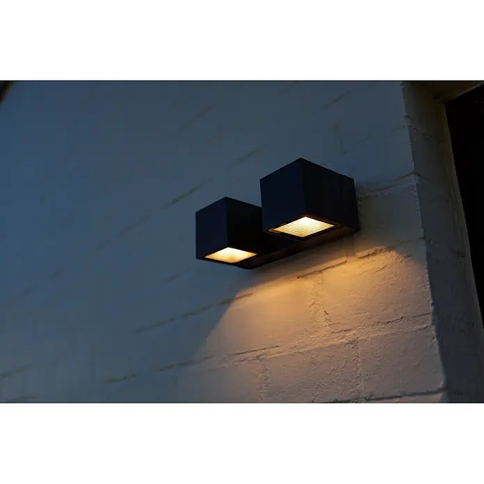 Lutec Aplique para exterior LED Fari - 10 W, L x An x Al: 92 x 65 x 193 mm, Gris oscuro, Aluminio, IP54 - Dos luces exteriores cúbicas negras montadas en una pared de ladrillo blanca, proyectando luz cálida.