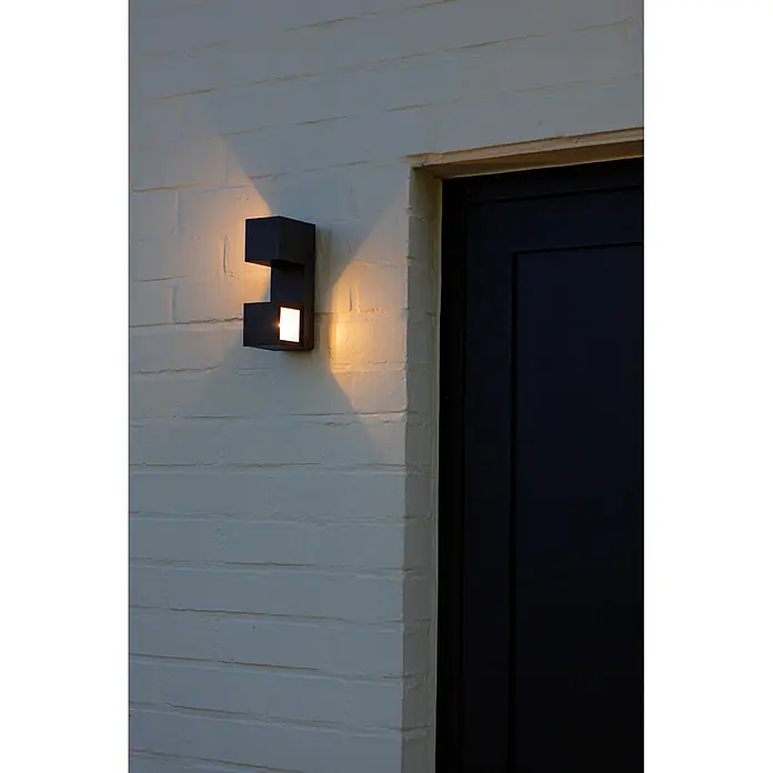 Lutec Aplique para exterior LED Fari - 10 W, L x An x Al: 92 x 65 x 193 mm, Gris oscuro, Aluminio, IP54 - Aplique de pared geométrico gris oscuro en pared de ladrillo, emitiendo luz cálida hacia arriba y abajo junto a una puerta oscura.