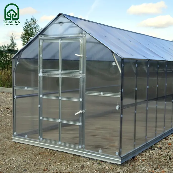 Klasika Greenhouses Gewächshaus Bernard Klasika - Außenmaß inkl. Dachüberstand (B x T): 235 x 600 cm, Material Seitenwand: Kunststoff, 6 mm, Silbergrau - Freistehendes Gewächshaus mit silbernem Metallrahmen und lichtdurchlässigen Paneelen, auf einem Kiesgrund im Freien.
