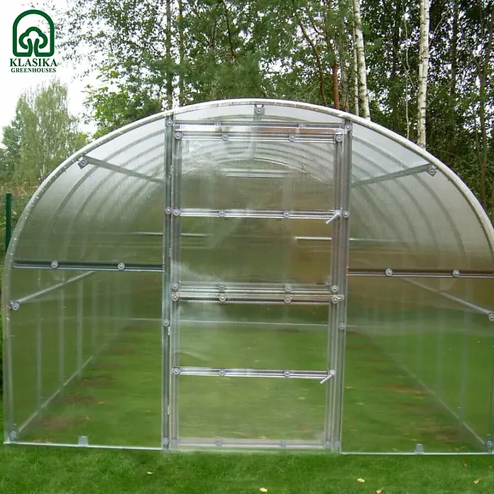 Klasika Greenhouses Gewächshaus Baltic Lt Klasika - Außenmaß inkl. Dachüberstand (B x T): 300 x 800 cm, Material Seitenwand: Kunststoff, 6 mm, Silbergrau - Transparentes Gewächshaus mit gewölbter Form und silbernem Metallrahmen auf grünem Rasen im Freien.