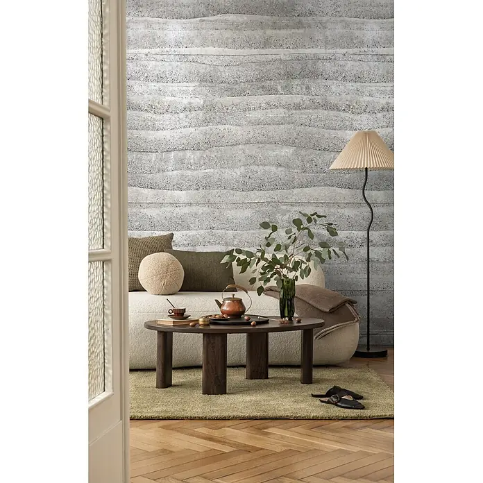 A.S. Création Metropolitan Stories Vibes & Styles Fototapete Beton I - B x H: 1,59 x 2,8 m, Vlies - Gemütliches Wohnzimmer mit hellem Bouclé-Sofa, dunklem Holztisch auf grünem Teppich und texturierter Betonwand.