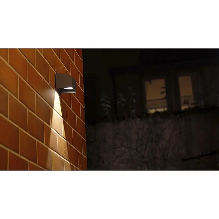 BAUHAUS LED-Solar-Außenwandleuchte Umea - 1,8 W, Aluminium, Warmweiß, Anthrazit - Dunkelgraue quadratische Außenleuchte beleuchtet nachts eine Ziegelwand, an deren Oberfläche montiert.