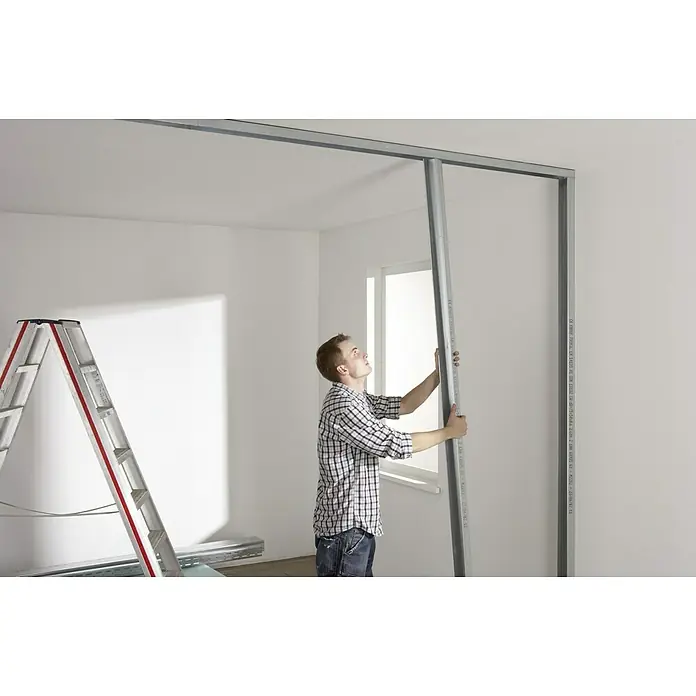 Knauf CW-Standprofil - 2.600 x 50 x 50 mm, Stahl - Ein Mann montiert eine Trockenbauwand in einem Raum. Die Metallkonstruktion ist gut sichtbar, eine Leiter steht im Hintergrund.