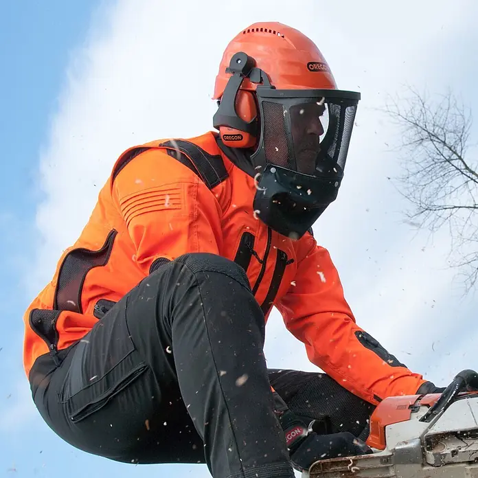Oregon Forst-Schutzhelm Waipoua - Universal - Person in orange-schwarzer Schutzkleidung mit Helm, Visier und Gehörschutz bedient eine Kettensäge, Holzspäne fliegen.
