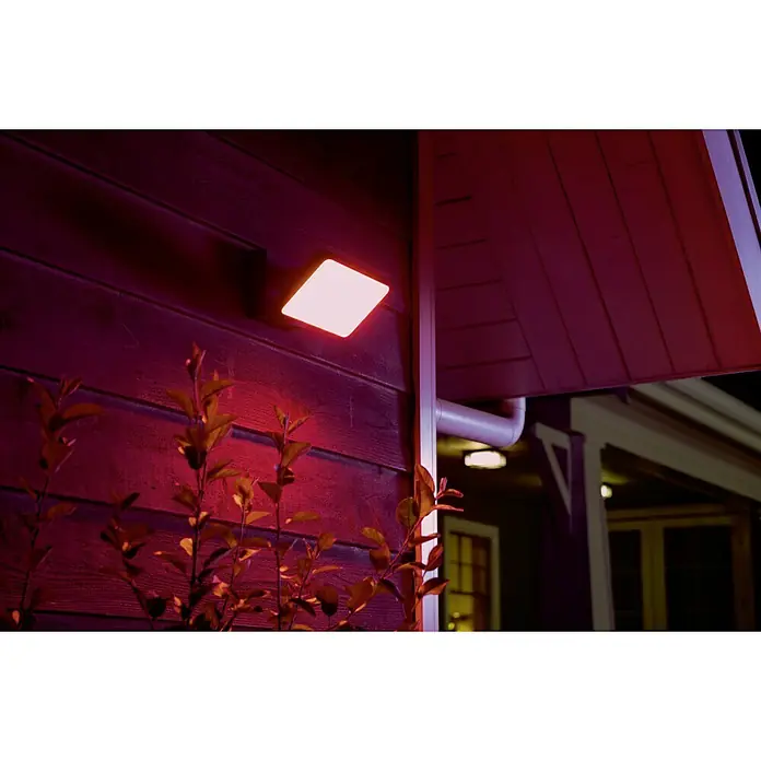 Philips Hue LED-Strahler White & Color Ambiance - 15 W, L x B x H: 22 x 16 x 15,3 cm, Schwarz, RGBW - Nahaufnahme einer Philips Hue LED Außenleuchte an einer Hauswand, die ein helles, farbiges Licht ausstrahlt und die Fassade beleuchtet.