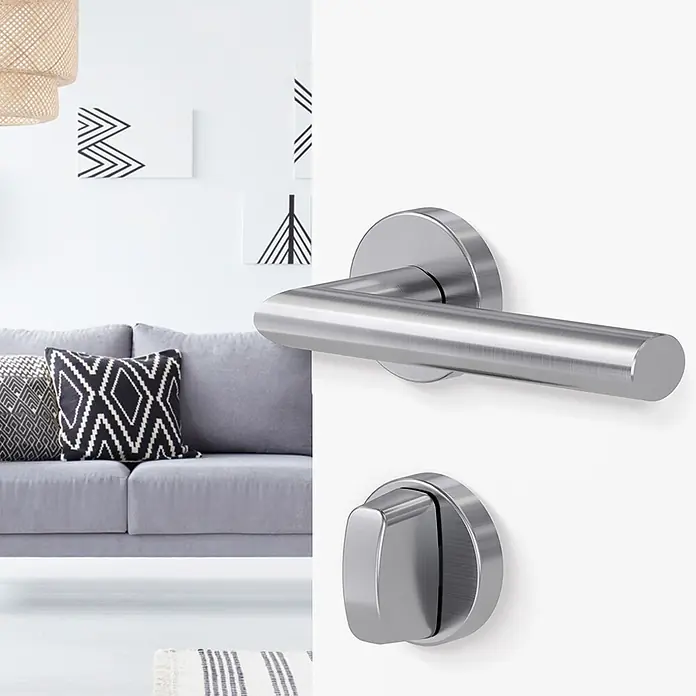 Diamond Doors Schlüsselschild - Durchmesser Rosette: 51 mm, Schlitzkopf/Olive, Samtgrau, Matt - Moderner Türdrücker und WC-Verriegelung aus gebürstetem Metall an einer Tür, mit Wohnzimmer im Hintergrund.