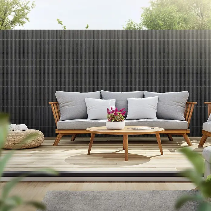ECD Germany Sichtschutzelement Anthrazit Windschutz Zaunblende für Garten Balkon Terrasse - B x H: 700 x 160 cm, Kunststoff, Anthrazit - Dunkelgrauer, lamellenförmiger Sichtschutz im Freien auf einer Terrasse hinter einem Sofa, der eine moderne Abgrenzung bietet.