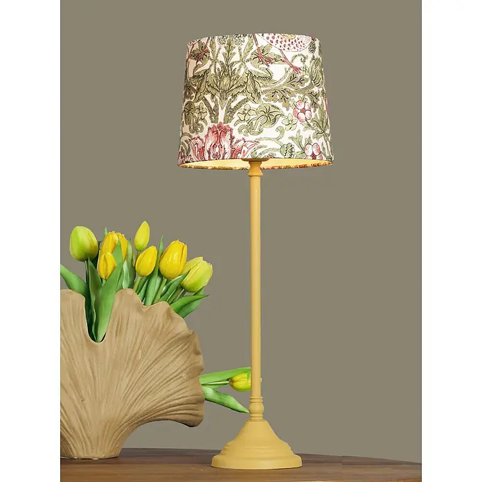 PR Home Tischleuchte Tove - 40 W, L x B x H: 20 x 20 x 57 cm, E27 - Tischlampe mit gelbem Fuß und gemustertem Schirm mit grünen Blättern und rosa Blumen, neben gelben Tulpen in einer Vase auf einem Holztisch.