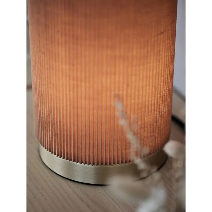 PR Home Tischleuchte Dora - 25 W, E27 - Tischleuchte mit orangefarbenem Faltenstoffschirm und gebürstetem Messingsockel auf einer hellen Holzoberfläche.