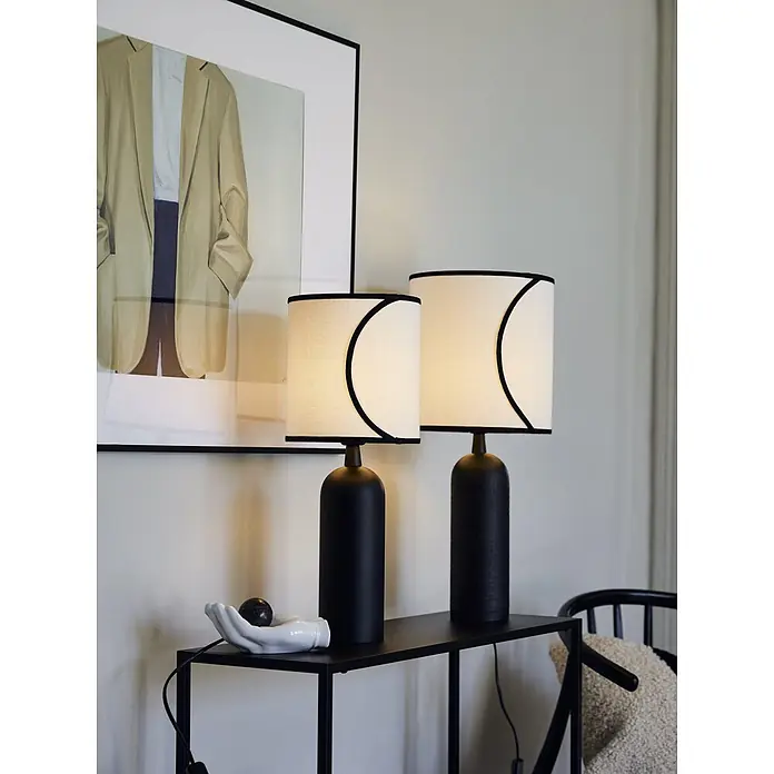 PR Home Tischleuchte Riley - 40 W, E27 - Zwei schwarze Tischlampen mit weißen Schirmen und schwarzer Zierleiste auf einem schwarzen Konsolentisch.