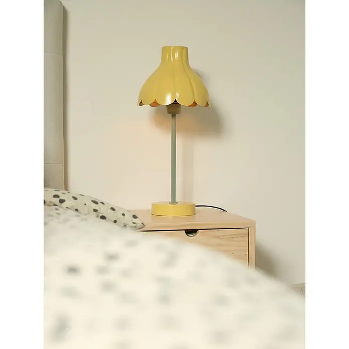 PR Home Tischleuchte Wera - 15 W, E27 - Gelbe blumenförmige Tischlampe auf einem Nachttisch aus Holz neben einem Bett.
