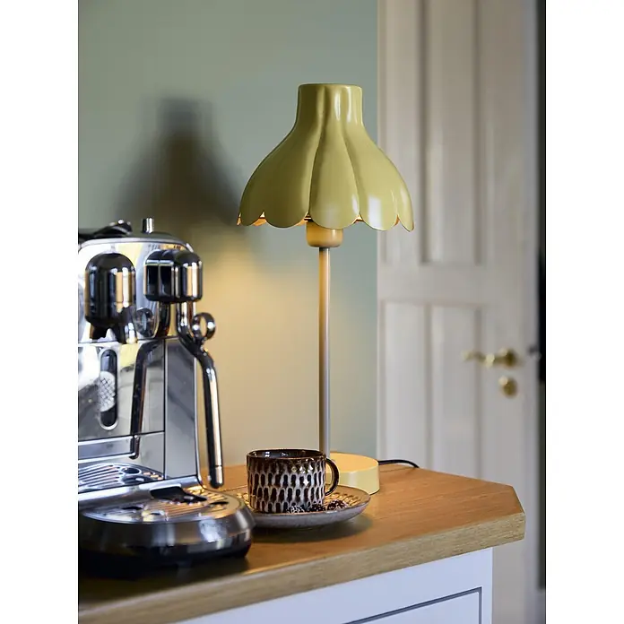 PR Home Tischleuchte Wera - 15 W, E27 - Gelbe Tischlampe mit gewelltem Schirm auf einer Holztheke neben einer Chrom-Kaffeemaschine und einer gemusterten Kaffeetasse mit Bohnen.