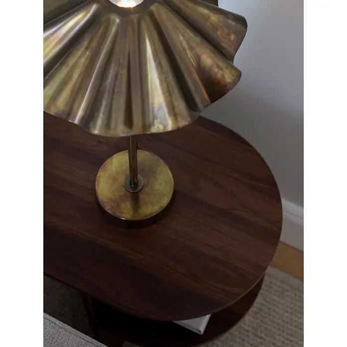 PR Home Tischleuchte 46cm - 25 W, E27 - Eine messingfarbene Tischlampe mit geriffeltem Schirm steht auf einem ovalen Beistelltisch aus dunklem Holz und spendet Licht.