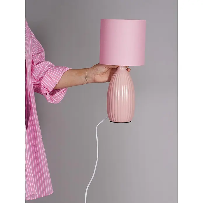 PR Home Tischleuchte Uno - 25 W, E14 - Eine Hand hält eine pinke Keramik-Tischlampe mit geripptem Fuß, passendem Lampenschirm und weißem Kabel.