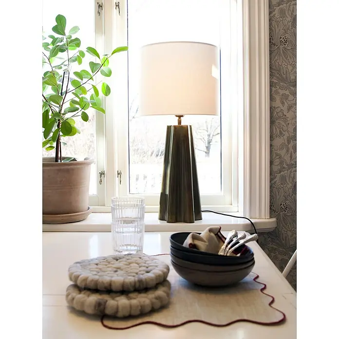 PR Home Tischleuchte 65cm - 40 W, E27 - Eine Tischlampe mit dunklem, facettiertem Sockel und hellem zylindrischem Schirm steht auf einer weißen Fensterbank.