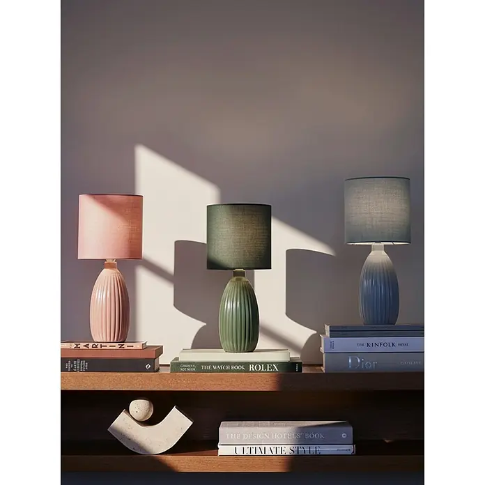 PR Home Tischleuchte Uno - 25 W, E14 - Drei Tischlampen mit gerippten Keramiksockeln und Stoffschirmen in Rosa, Grün und Blau, auf einem Holzregal mit Büchern präsentiert.