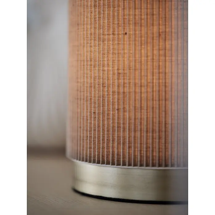 PR Home Tischleuchte Dora - 25 W, L x B x H: 14 x 14 x 25 cm, E27 - Nahaufnahme einer beleuchteten Lampe mit plissiertem Stoffschirm und gebürstetem Messingsockel auf Holzfläche.