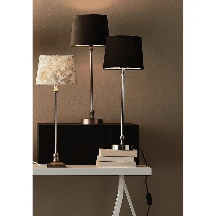 PR Home Tischleuchte Liam - 40 W, E27 - Drei elegante Tischlampen mit Metallfüßen und Stoffschirmen, zwei schwarz und einer floral, auf weißem Tisch und schwarzer Box.