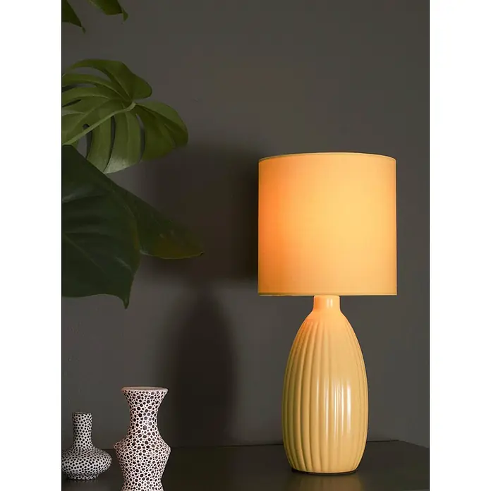 PR Home Tischleuchte Uno - 60 W, E14 - Eine beleuchtete gelbe Tischlampe mit gerilltem Keramikfuß und passendem Stoffschirm, die ein warmes Licht spendet.