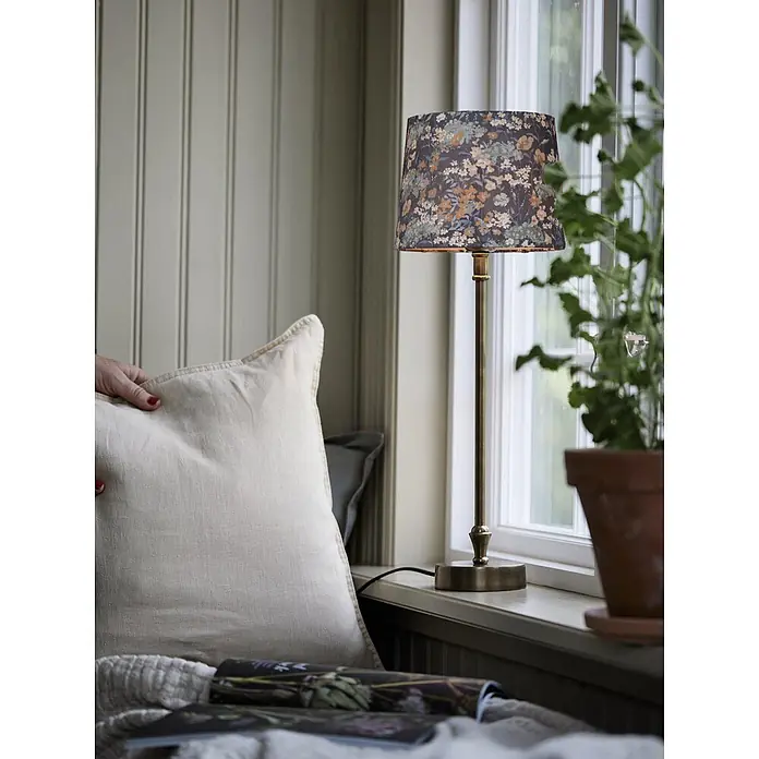 PR Home Tischleuchte Liam - 40 W, L x B x H: 20 x 20 x 56 cm, E27 - Tischlampe mit messingfarbenem Fuß und dunklem floralem Lampenschirm, auf einer Fensterbank platziert.