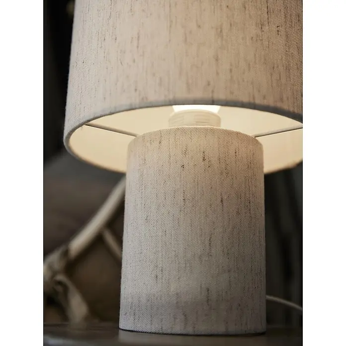 PR Home Tischleuchte Leah - 15 W, E27 - Nahaufnahme einer eingeschalteten Tischlampe mit hellbeigem Stoffschirm, die warmes Licht abgibt.