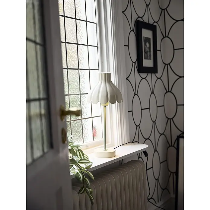 PR Home Tischleuchte Wera - 25 W, E27 - Eine dekorative Tischlampe mit gewelltem cremefarbenem Schirm und hellgrünem Ständer steht auf einem Fensterbrett und spendet Licht.