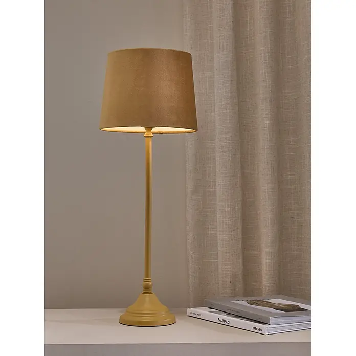 PR Home Tischleuchte Tove - 40 W, L x B x H: 20 x 20 x 57 cm, E27 - Beleuchtete senfgelbe Tischlampe mit Stoffschirm, auf einem Regal mit Büchern.