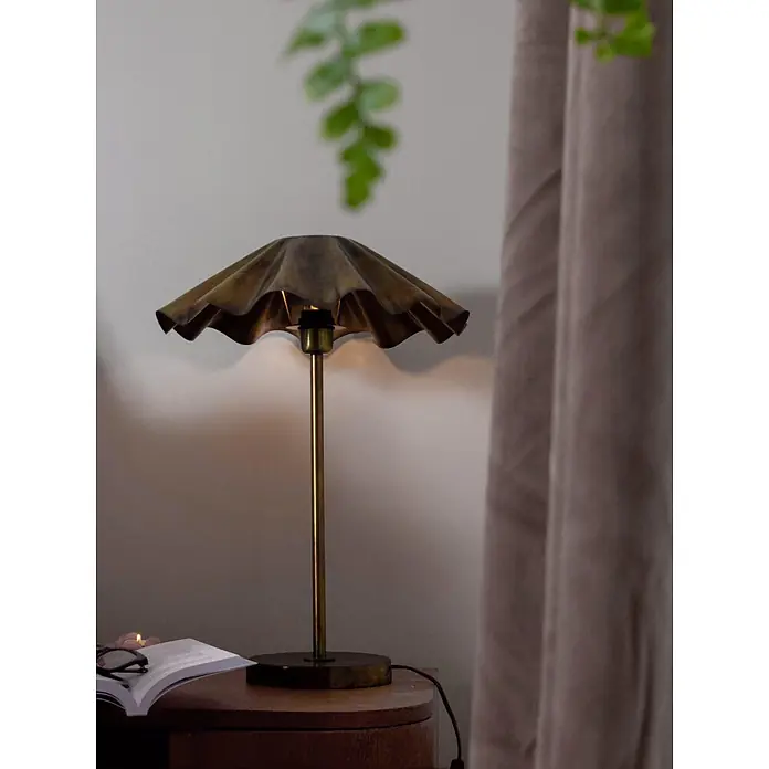 PR Home Tischleuchte Aira - 25 W, E27 - Messing-Tischlampe mit Rüschenschirm spendet warmes Licht auf einem Holztisch neben einem offenen Buch.