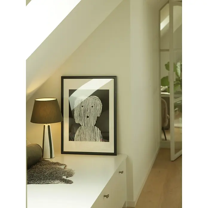 PR Home Tischleuchte Leya - 25 W, E27 - Beleuchtete Tischlampe mit dunkelgrünem Schirm und gestreiftem Fuß, neben einem gerahmten S/W-Kunstdruck auf einem weißen Schrank.