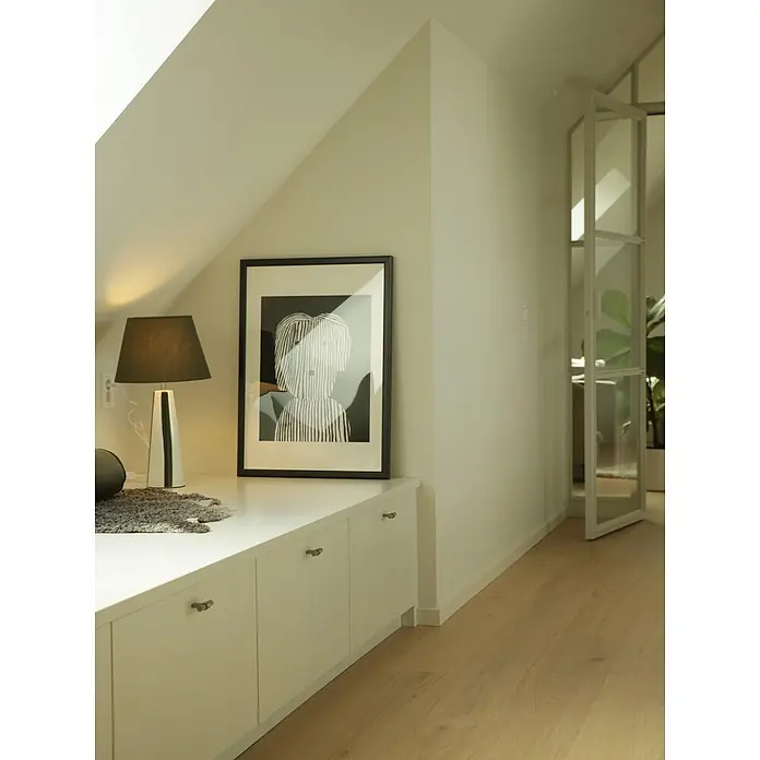 PR Home Tischleuchte Leya - 25 W, E27 - Helles Dachzimmer mit weißer Einbaubank, abstraktem Kunstbild, Lampe und hellem Holzboden, führt zu einer Tür mit Glasscheiben.