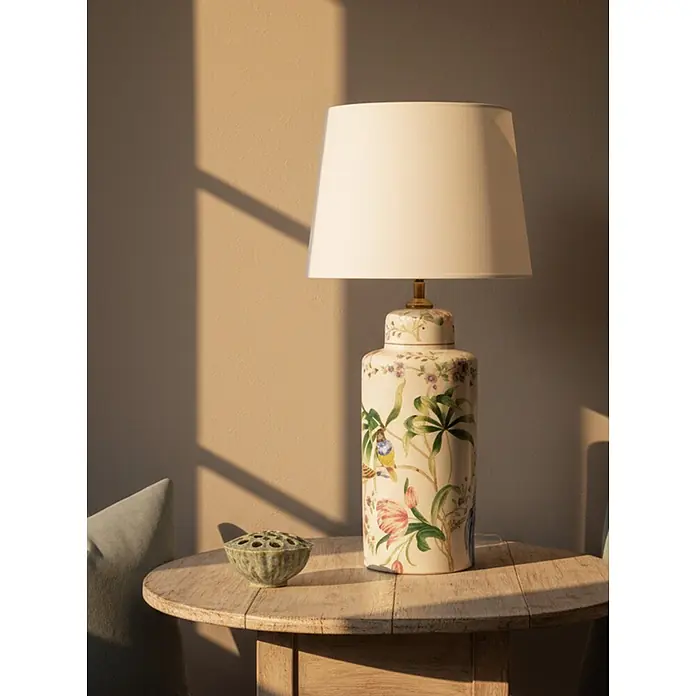 PR Home Tischleuchte - 40 W, E27 - Elegante Keramik-Tischlampe mit floralen Mustern und Vogeldarstellungen, weißem Schirm, von natürlichem Licht auf Holztisch beleuchtet.