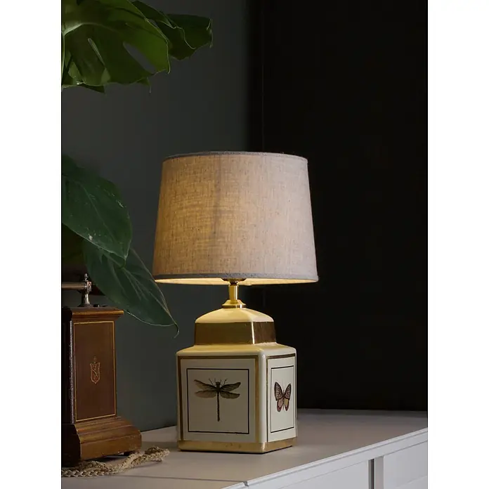 PR Home Tischleuchte Lucca - 40 W, E27 - Tischleuchte mit beigem Stoffschirm und weiß-goldener Keramikbasis mit Libellen- und Schmetterlingsmotiv, die warmes Licht spendet.