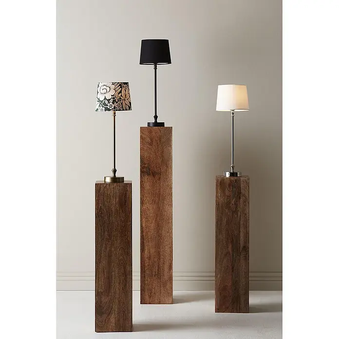 PR Home Tischleuchte Liam - 15 W, E27 - Drei Tischlampen mit verschiedenen Schirmen (geblümt, schwarz, weiß) und Metallsockeln (Messing, schwarz, Chrom) auf dunklen Holzpodesten unterschiedlicher Höhe.