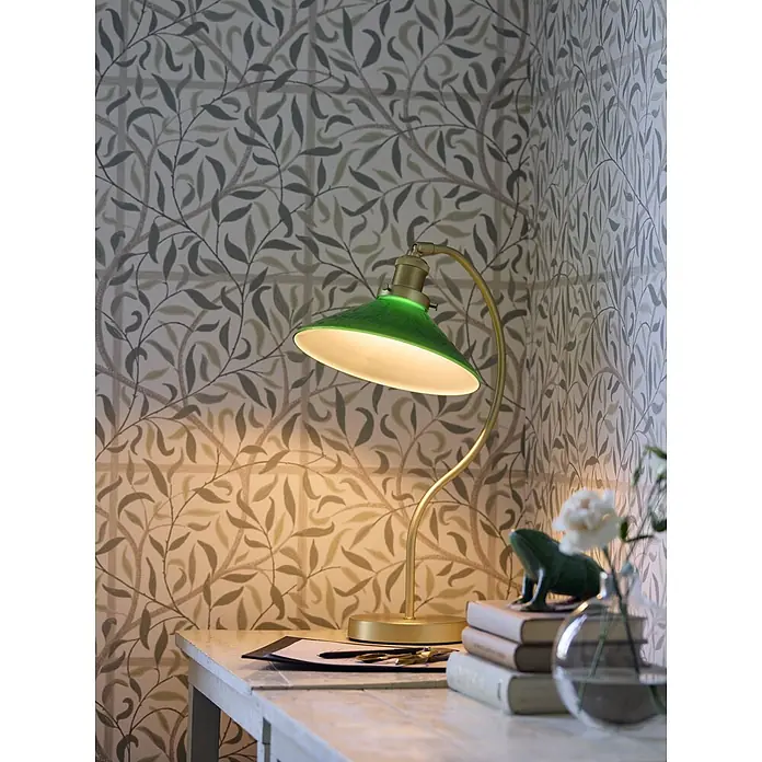 PR Home Tischleuchte Axel - 15 W, E27 - Grüne und goldene Schreibtischlampe beleuchtet einen Holztisch vor gemusterter Tapete.