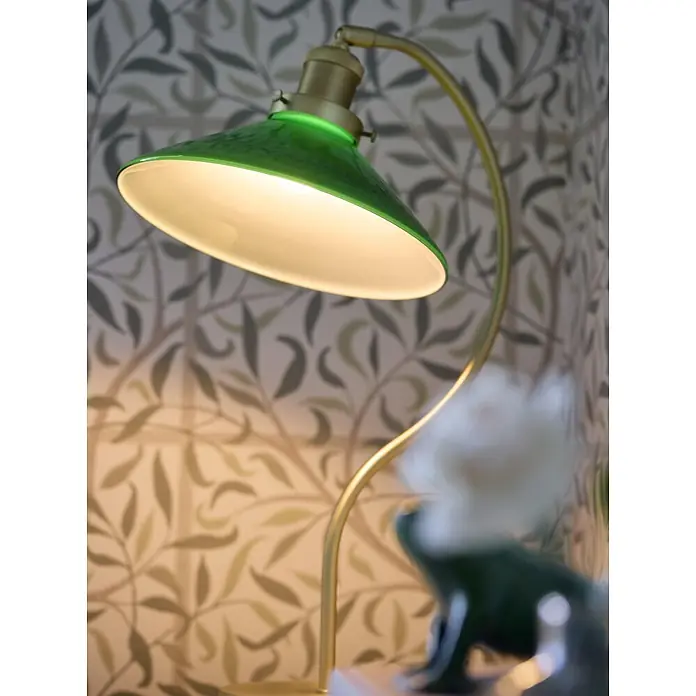 PR Home Tischleuchte Axel - 15 W, E27 - Eine moderne Tischlampe mit grünem Schirm und Messingfuß, die warmes Licht auf gemusterte Tapeten wirft.